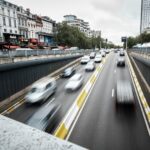 A group of cars driving down a street next to tall buildings