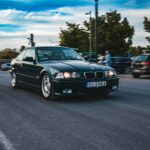 a black car driving down a street next to parked cars